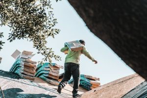 affordable roofing contractors in Greensboro: A person carrying a bundle of shingles across a residential roof
