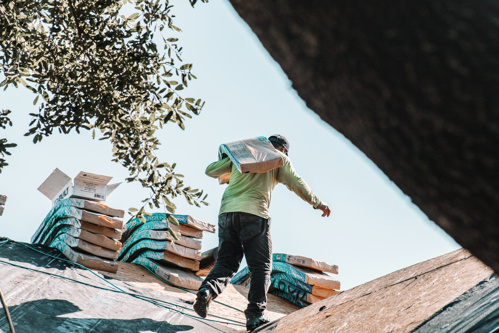 affordable roofing contractors in Greensboro: A person carrying a bundle of shingles across a residential roof